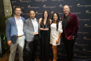 Five people in business attire pose with two crystal awards in front of a myhomegroup backdrop.